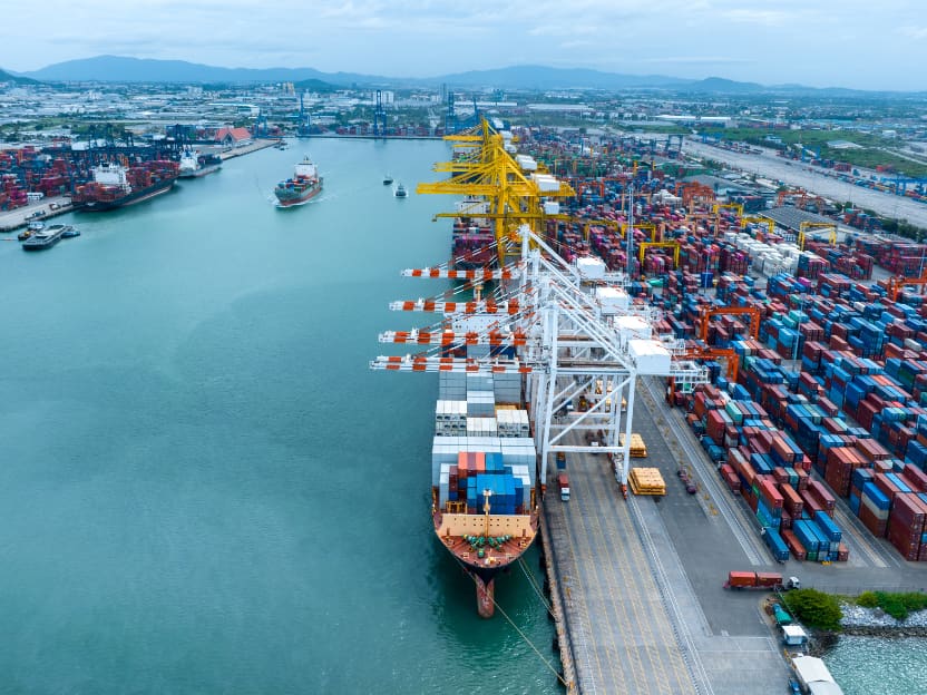 Aerial view of a container terminal, with gantry cranes working a container ship berthed alongside stacked containers.